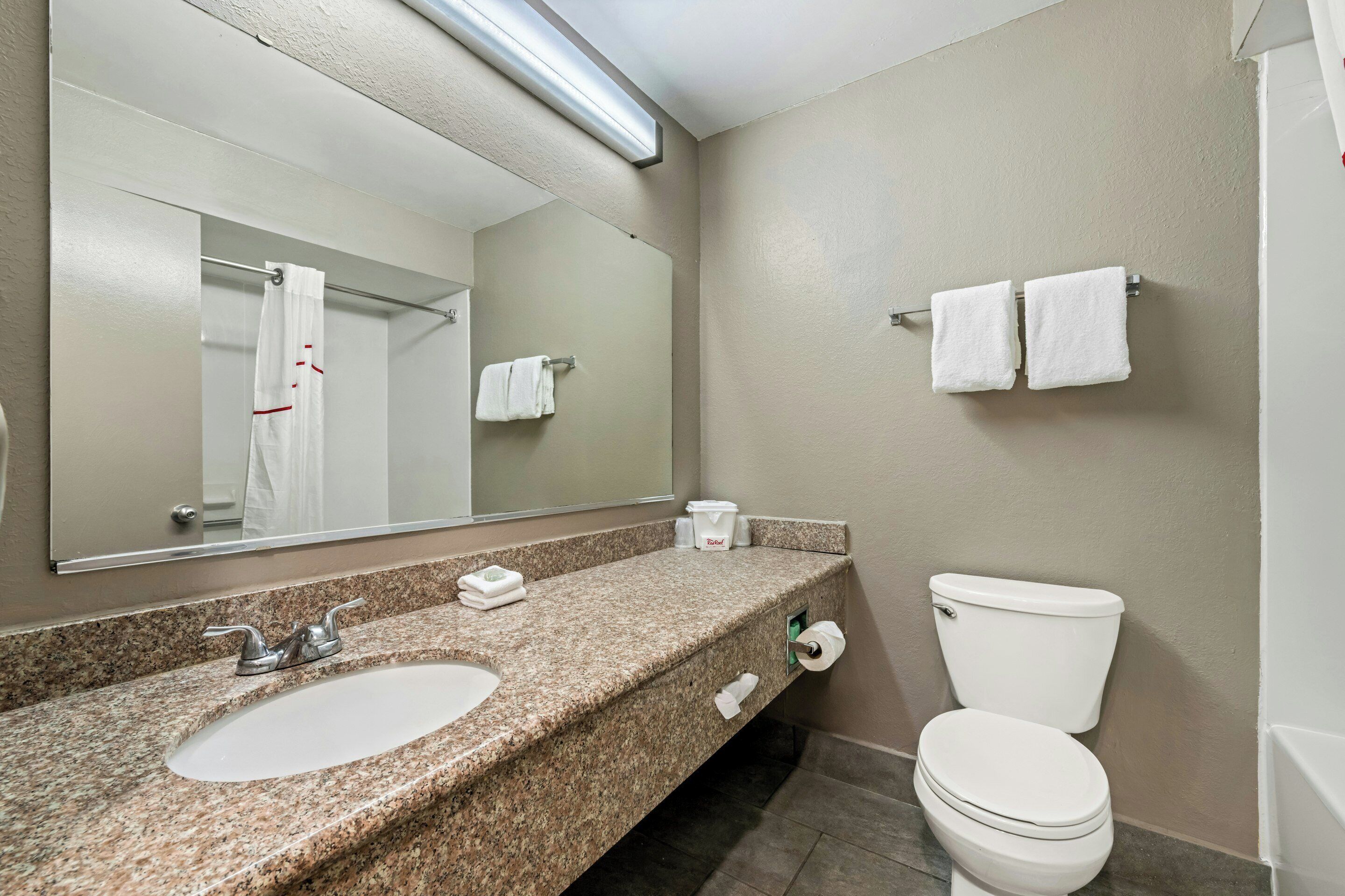 A bathroom with a granite countertop, a white sink, a mirror, a toilet, and a towel rack.