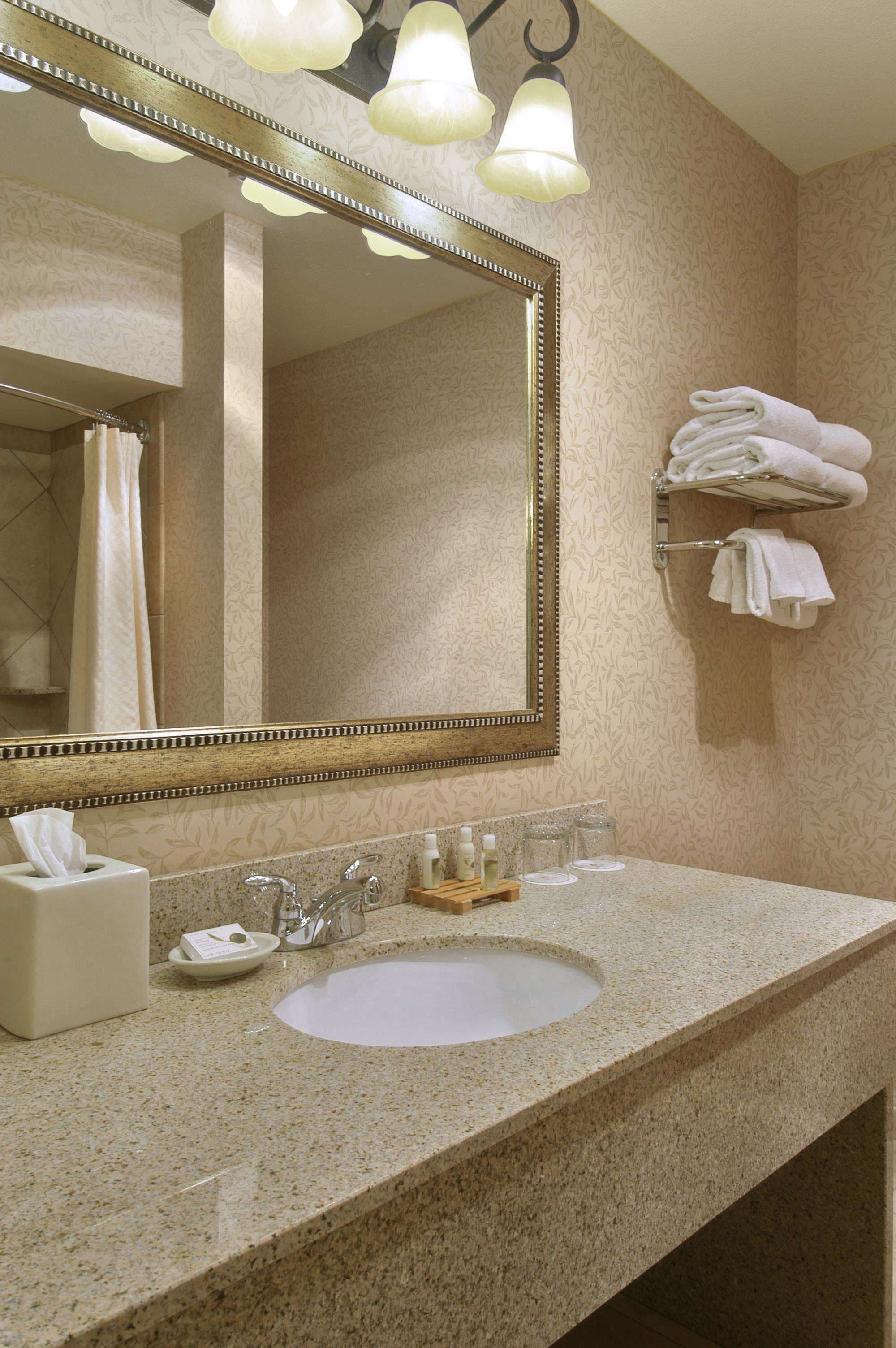 A bathroom with a granite countertop, a white sink, a large mirror, and a towel rack with folded towels.