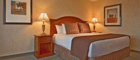 A hotel room with a large bed, two bedside tables with lamps, a nightstand, and two framed pictures on the walls.