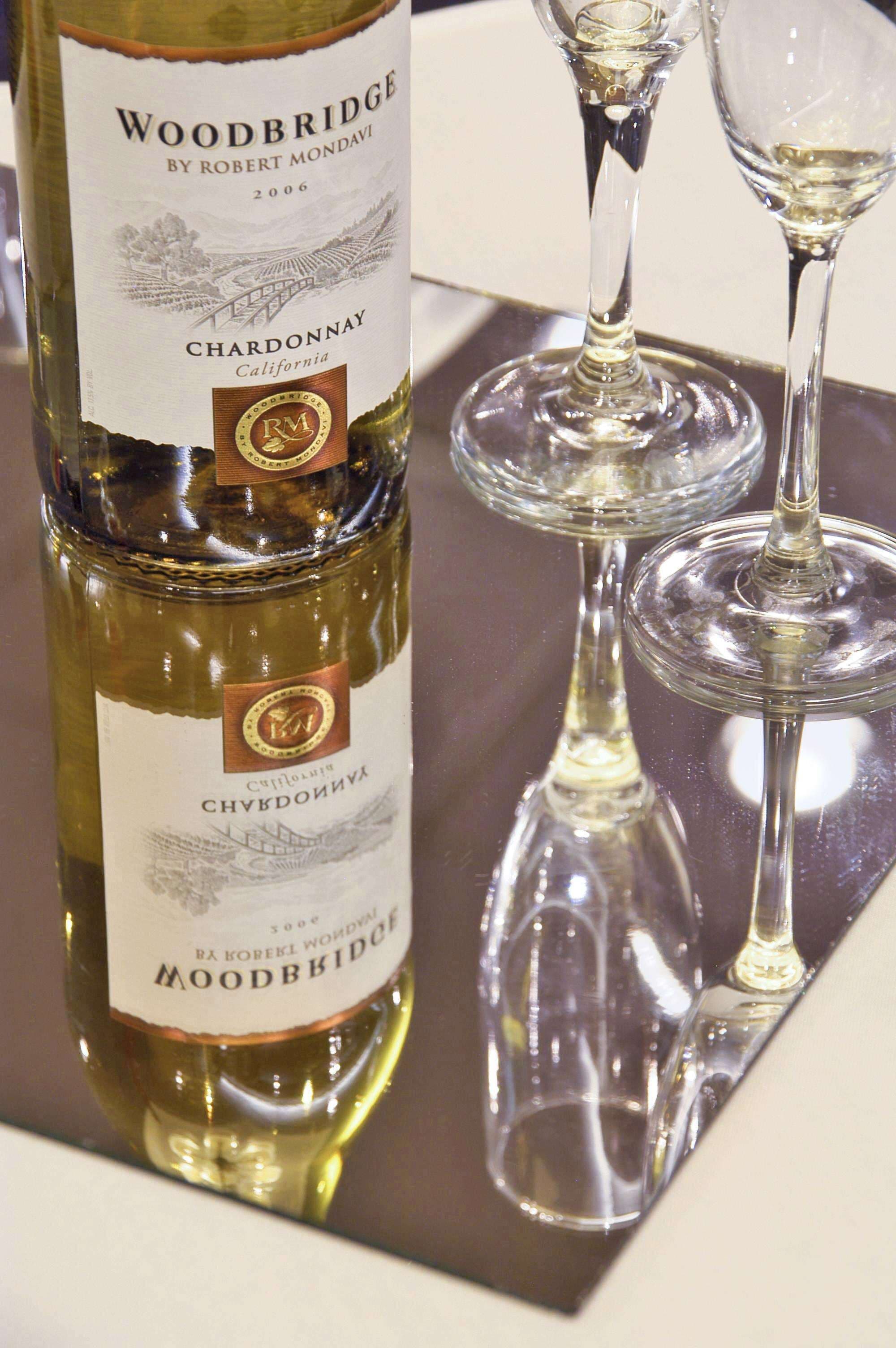 A bottle of Woodbridge Chardonnay and two empty wine glasses on a reflective surface.