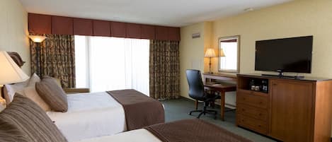 A hotel room with two beds, a desk, a television, and a chair.