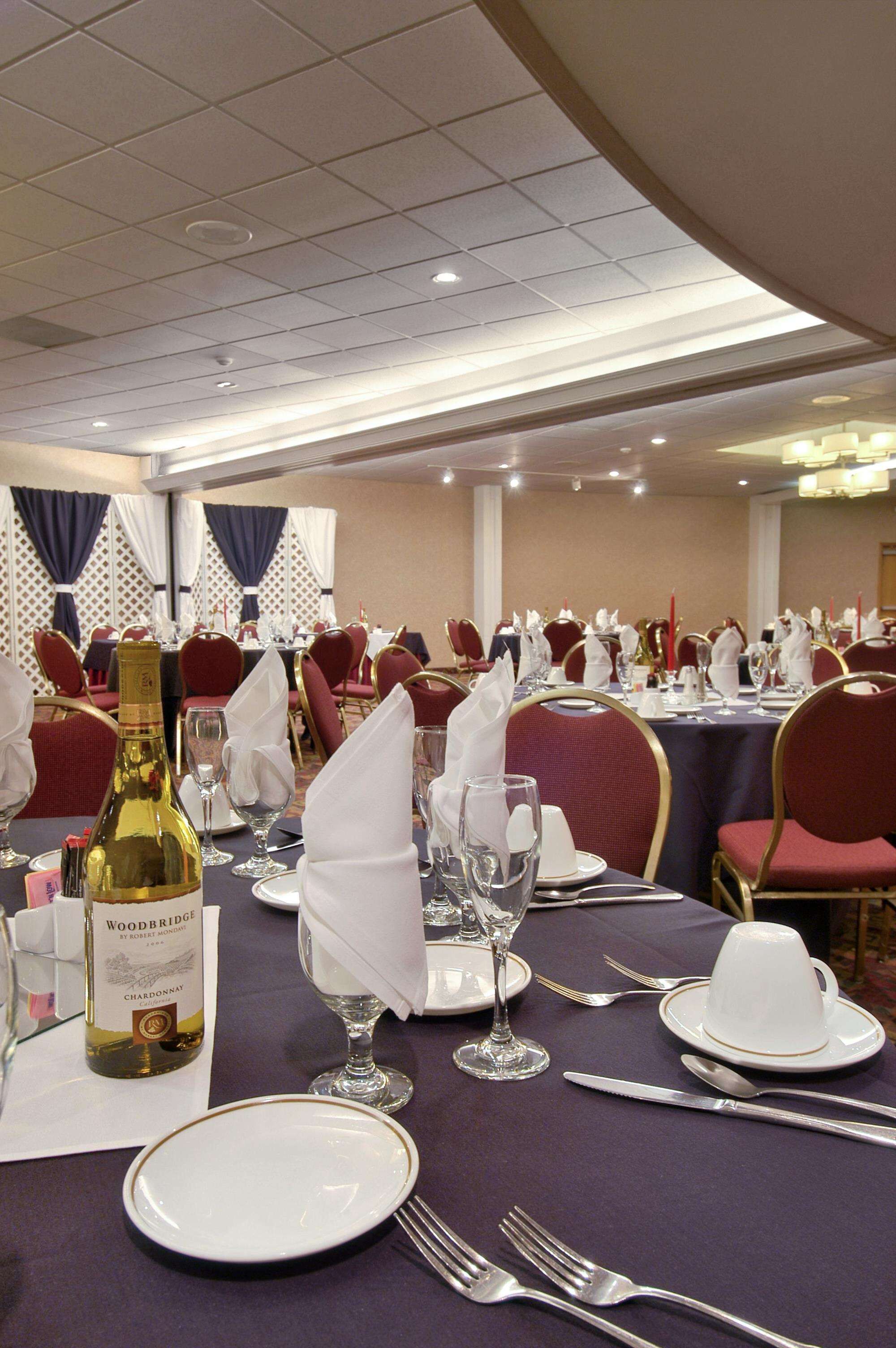 A banquet hall with tables set for dining, featuring white plates, silverware, and wine glasses.