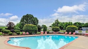 Una piscina rectangular con borde de ladrillo rojo, rodeada por una terraza pavimentada. Varias tumbonas rojas y blancas están dispuestas a lo largo de la piscina.