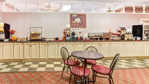 Un área de desayuno con bufé, máquinas de café y una mesa de comedor con sillas.
