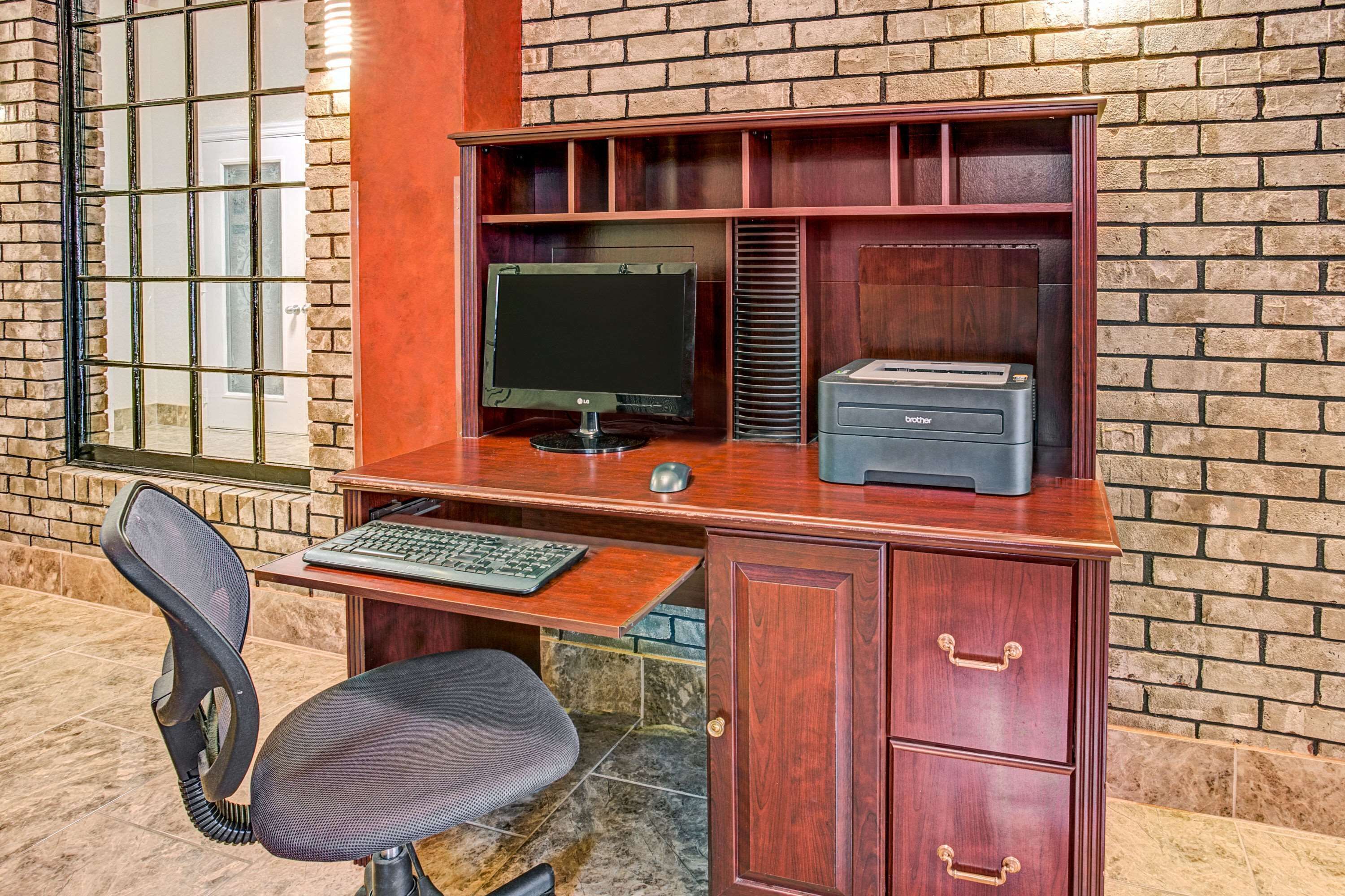 Una scrivania in legno con un computer, una stampante e una sedia da ufficio in una stanza con pareti in mattoni.