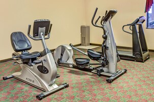 Un gimnasio con bicicletas estáticas, cintas de correr y un espejo grande.