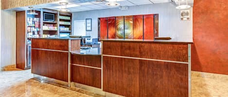 A reception area with a wooden reception desk, a digital screen, and a wall with a patterned design.