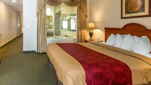 A hotel room with a large bed, a bedside table with a lamp, a mirror, and a bathroom visible through a door. - Econo Lodge Inn & Suites Riverside - Corona (Riverside)