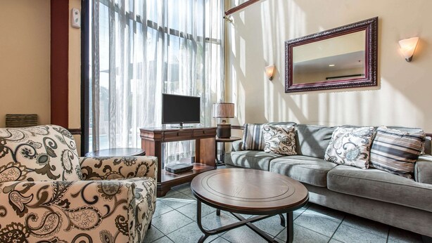 A living room with a sofa, armchair, and coffee table, a flat-screen TV, and a large window with sheer curtains. - Econo Lodge Inn & Suites Riverside - Corona (Riverside)