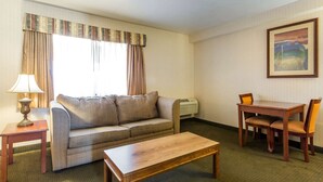 A hotel room with a sofa, a wooden coffee table, a dining table with chairs, a lamp, and a painting on the wall. - Econo Lodge Inn & Suites Riverside - Corona (Riverside)