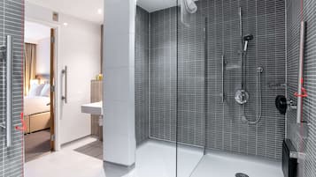 A modern bathroom with a glass shower enclosure, a white sink, and a beige bath area.