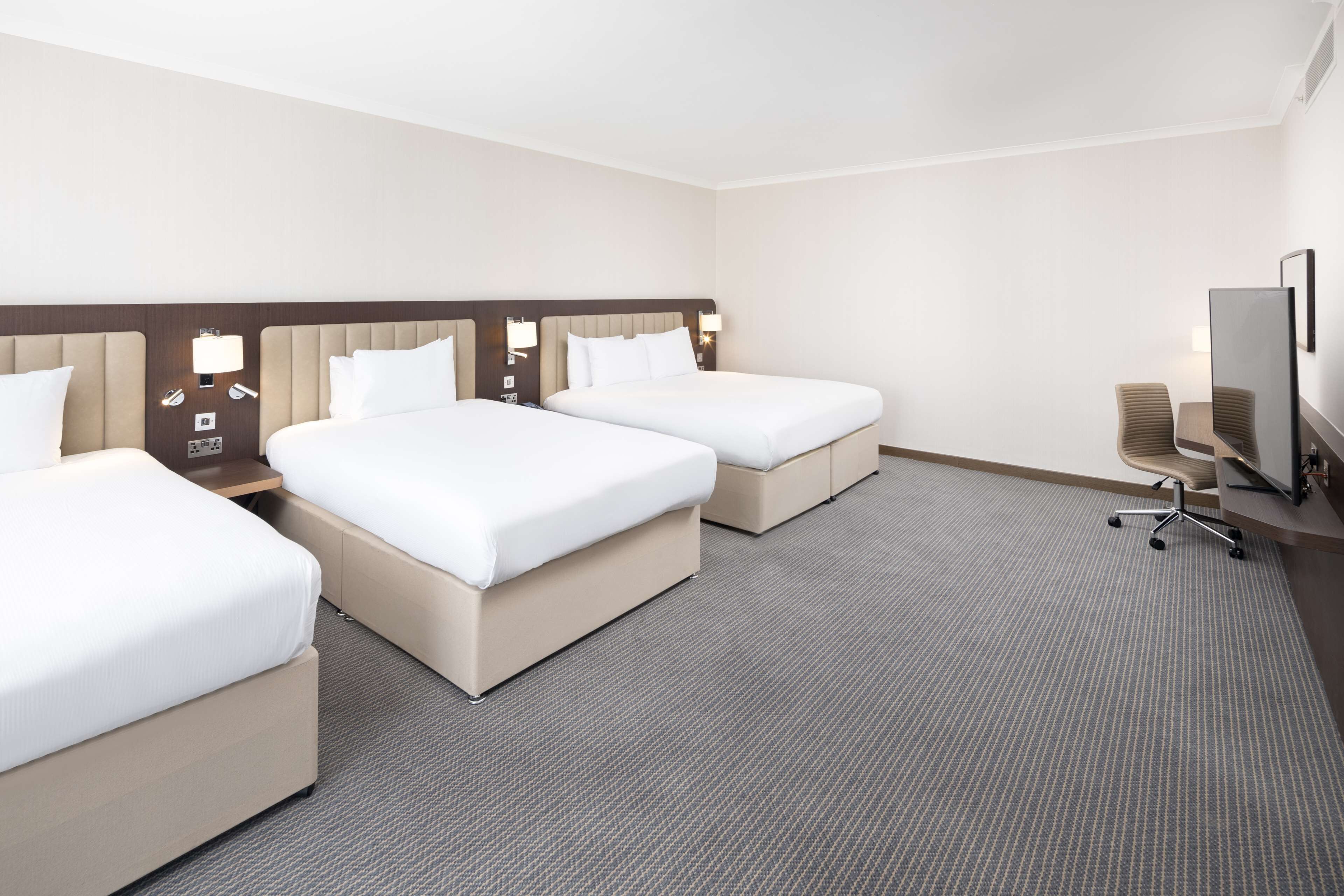 A hotel room with three beds, a television, and a desk with a chair.