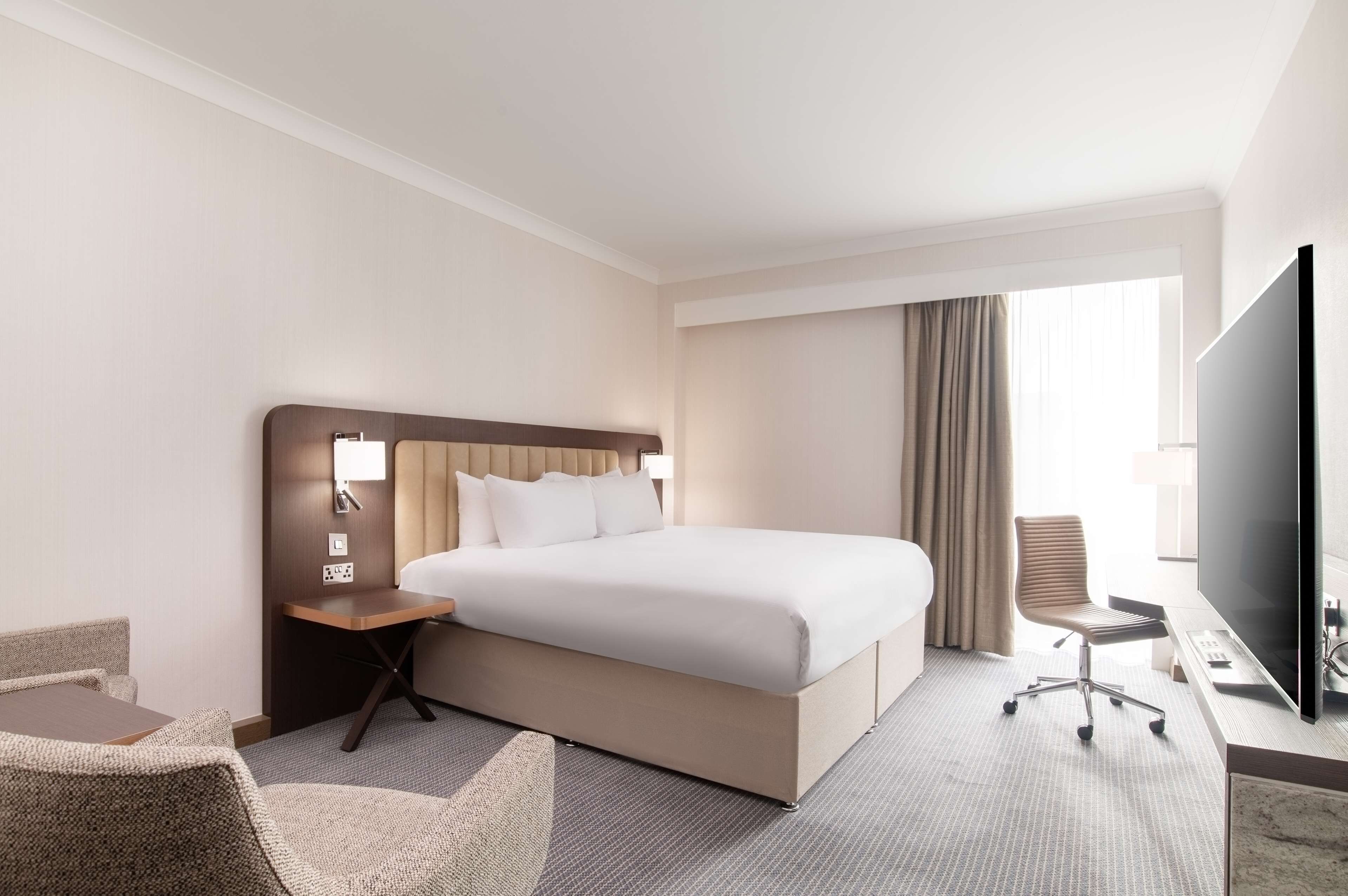 Hotelkamer met een groot bed, een bureau met stoel, een televisie en een raam met gordijnen.
