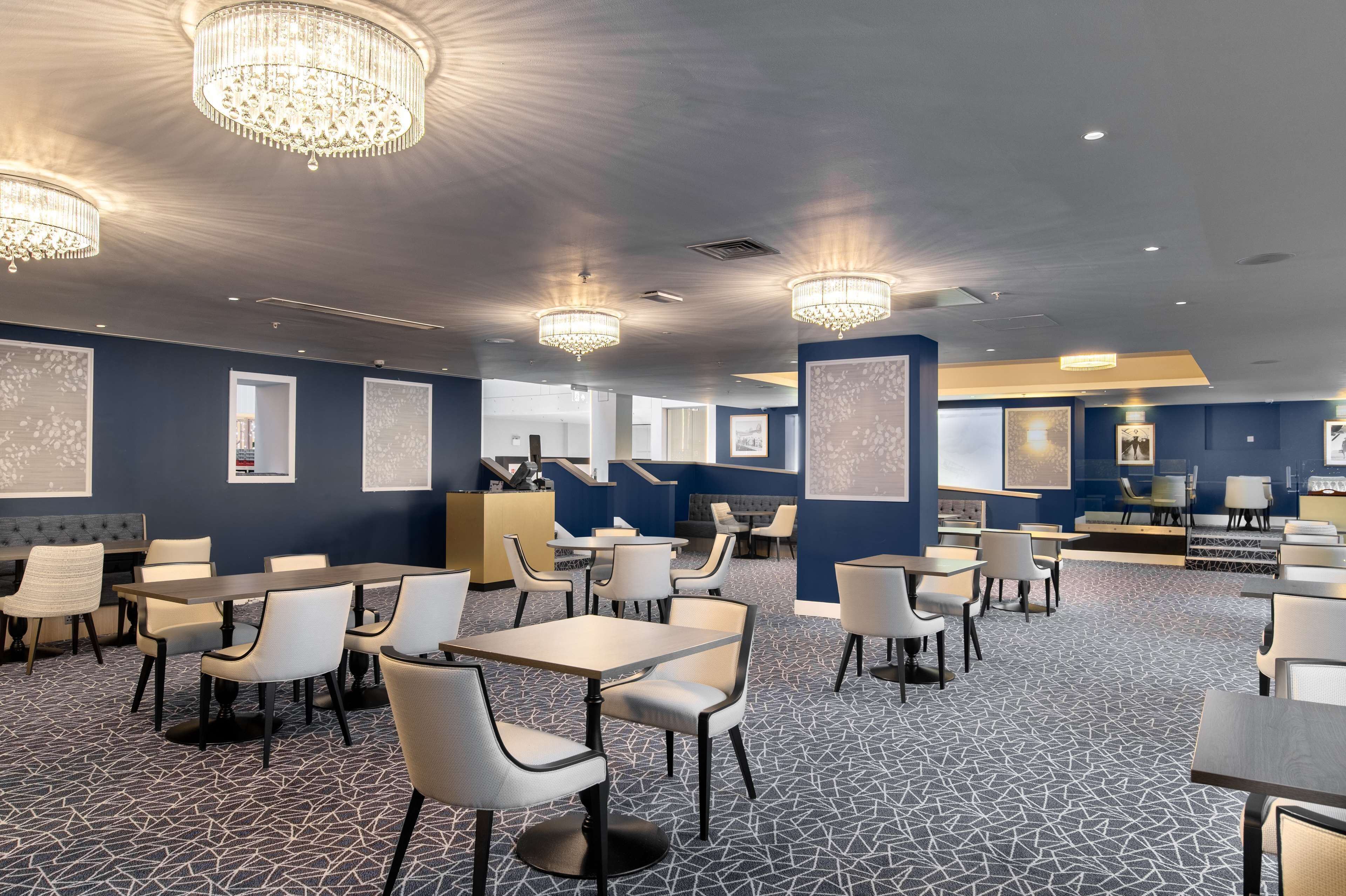 A spacious hotel lobby with multiple seating areas, chandeliers, and framed artwork on the walls.
