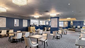 A spacious hotel lobby with multiple seating areas, chandeliers, and framed artwork on the walls.