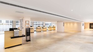 A spacious hotel lobby with a reception desk, multiple check-in counters, and framed artwork on the walls.
