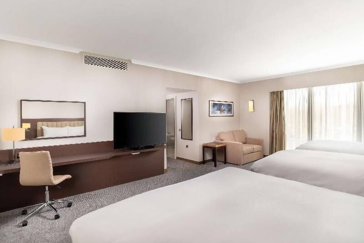 Hotellihuone, jossa on sänky, työpöytä tuolilla, televisio, pieni pöytä ja sohva.