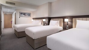 A hotel room with three beds, a wooden door, a framed picture on the wall, and a ceiling vent.