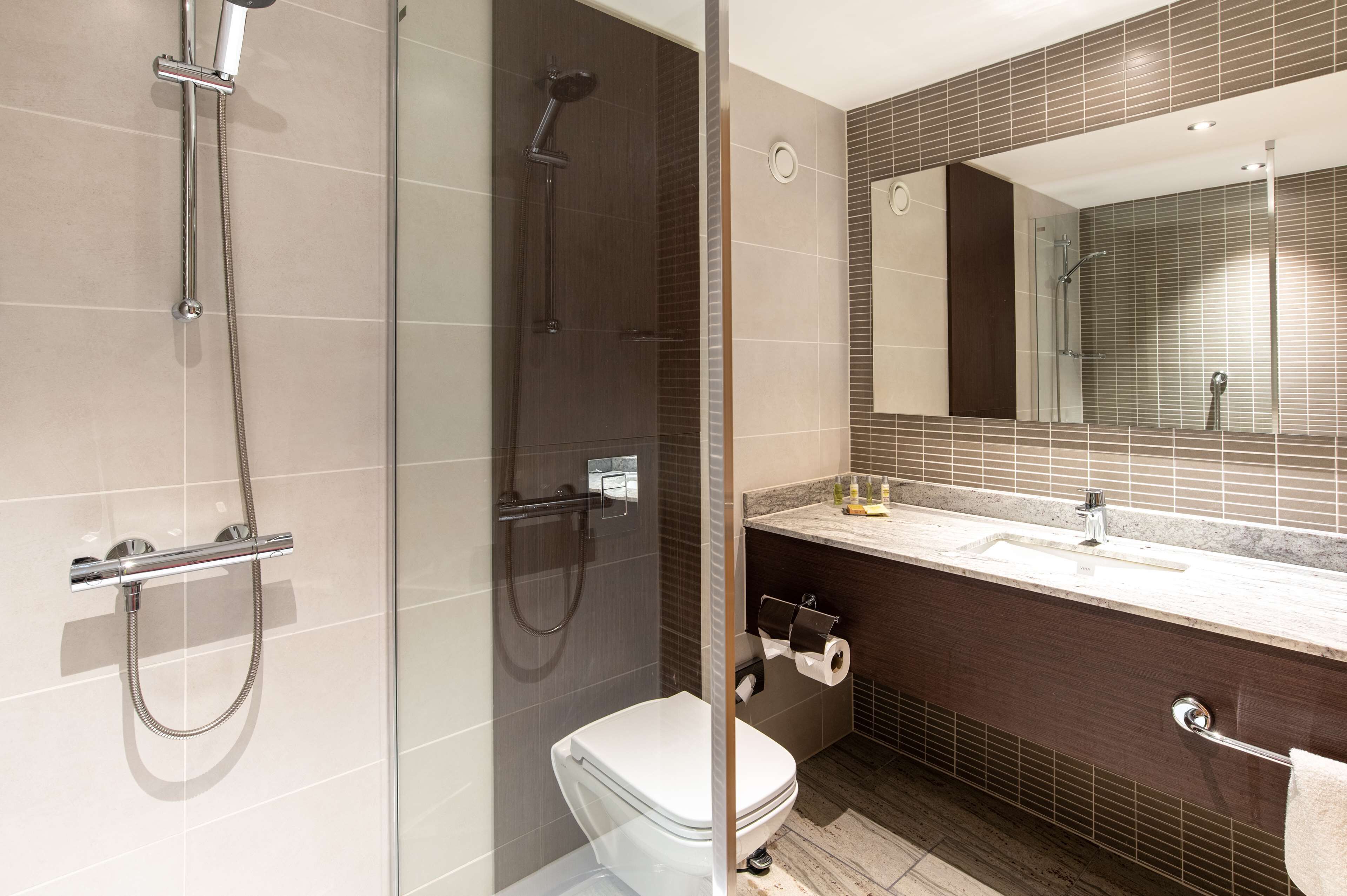 Un bagno moderno con doccia vetrata, un water bianco e un mobile lavabo con specchio e lavandino.