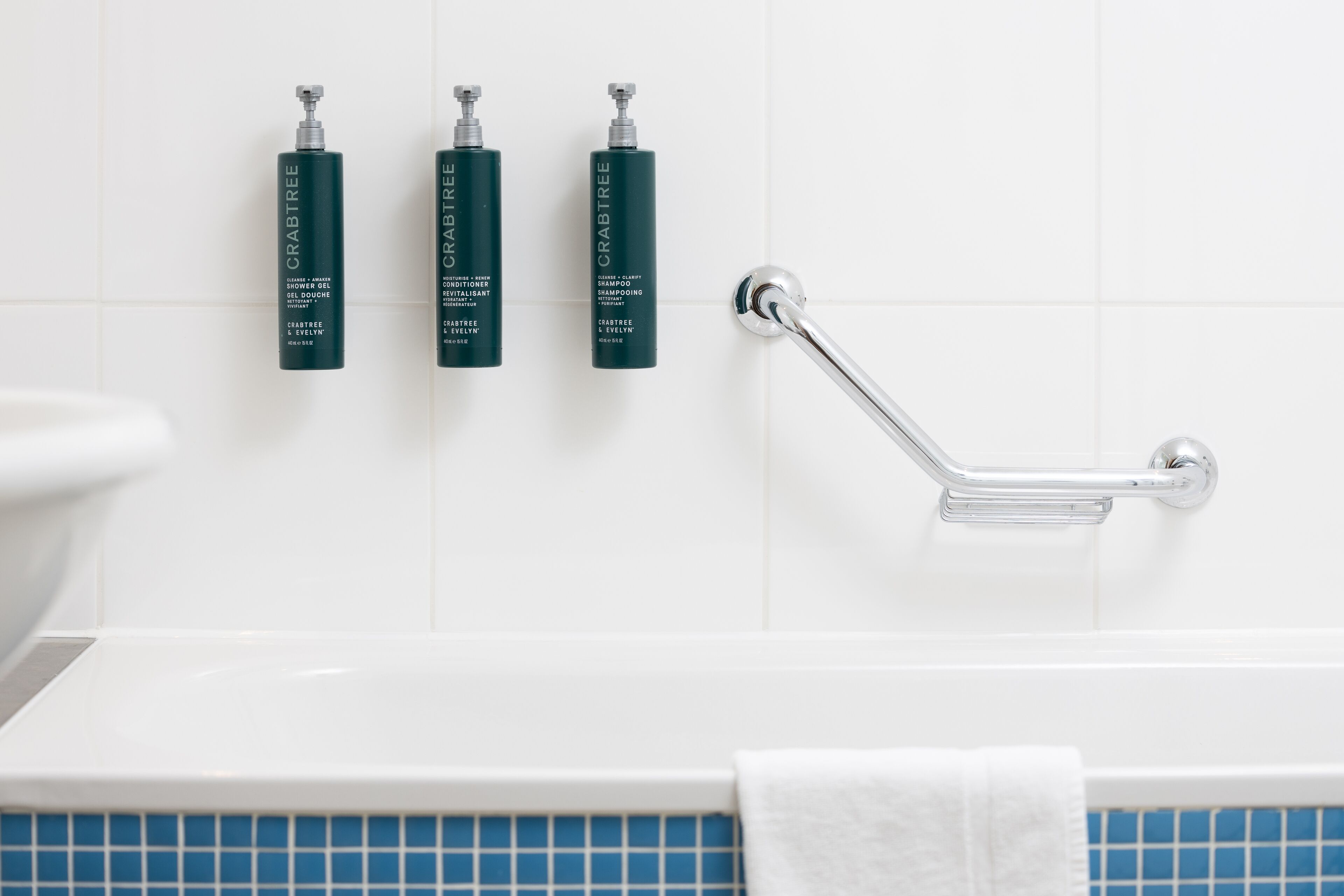 A bathroom with a white bathtub, a white toilet, and three bottles of Crabtree shower gel, conditioner, and shampoo on the wall.