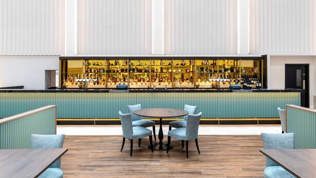 A bar area with a long counter displaying various bottles, a round table with chairs, and a green upholstered bench.