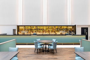 Een bar met een lange toonbank vol verschillende flessen, een ronde tafel met stoelen en een groene gestoffeerde bank.
