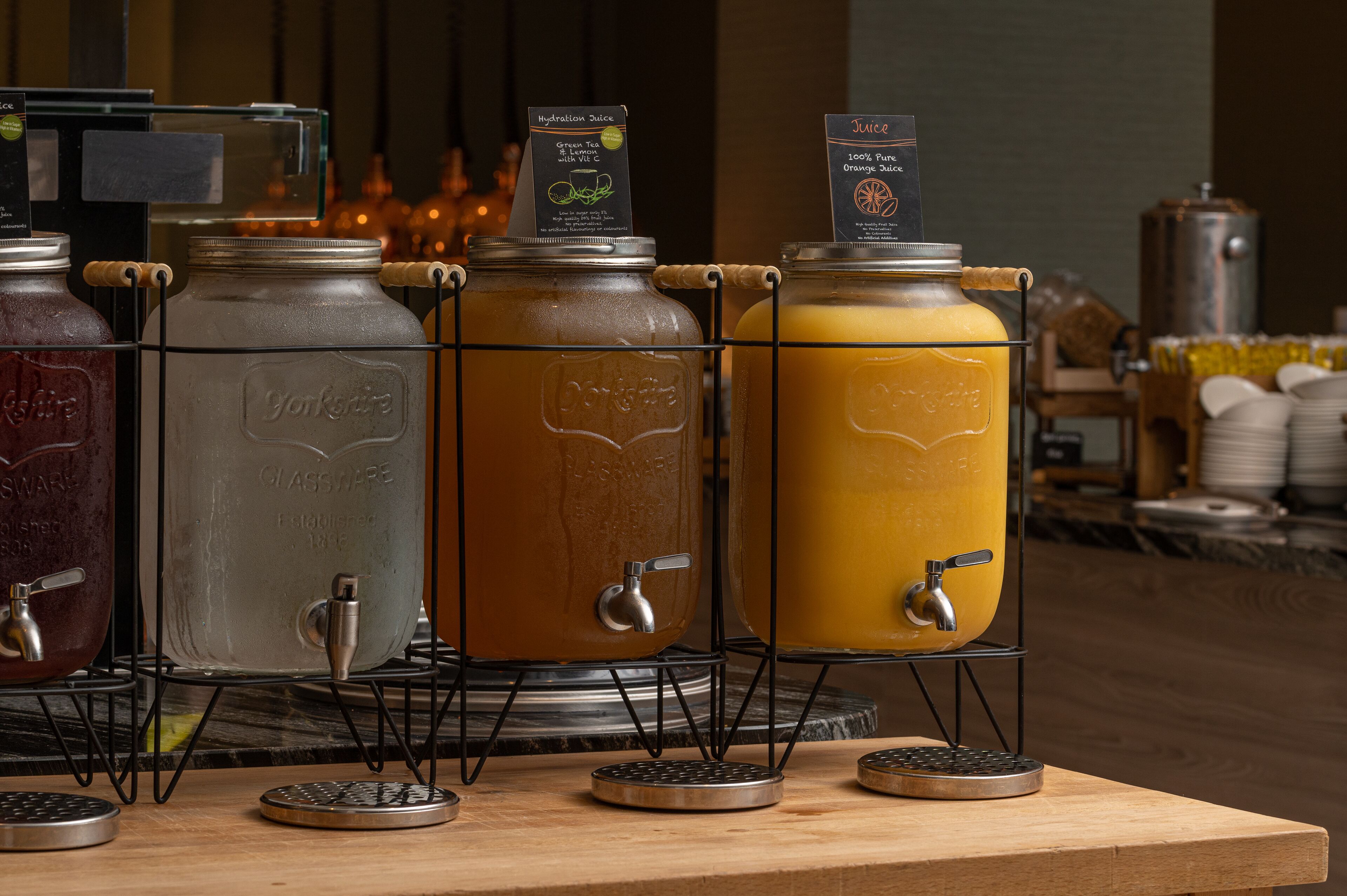 Uma estação de bebidas com vários dispensadores, incluindo chá verde e sumo de laranja.