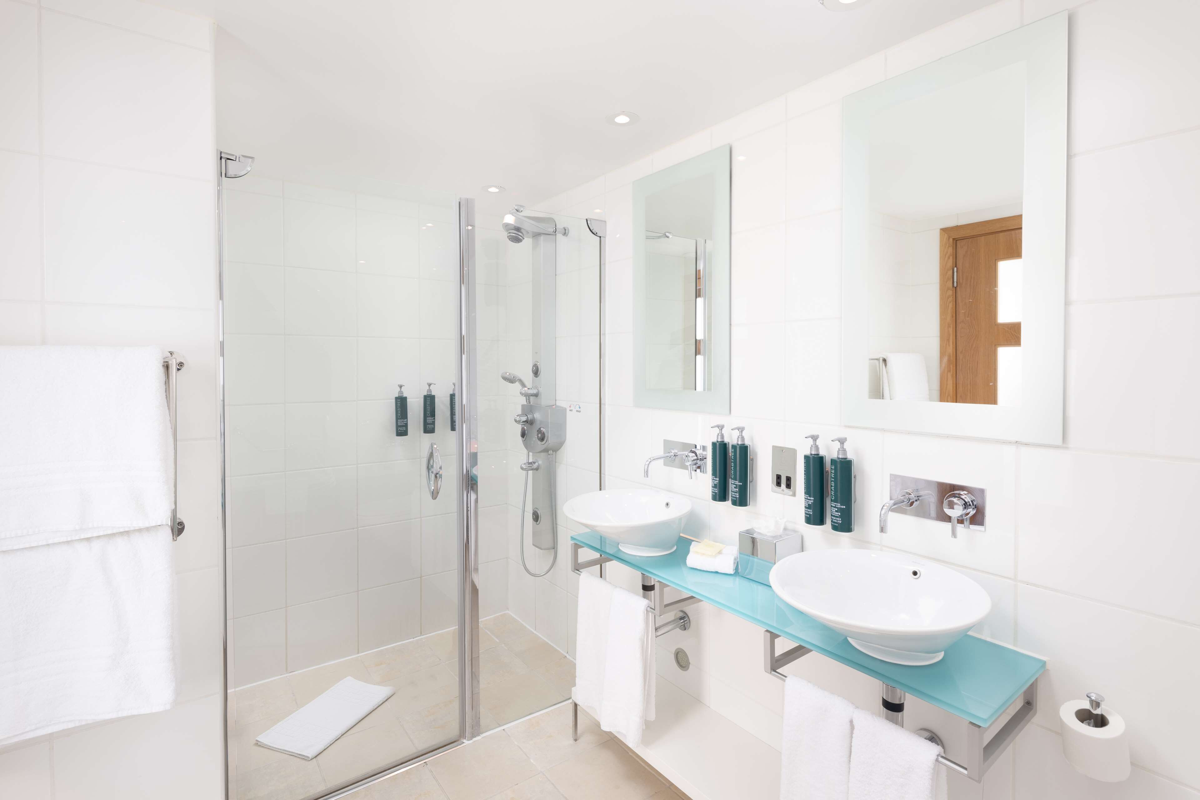 A modern bathroom with a glass-enclosed shower, two sinks, and a large mirror.