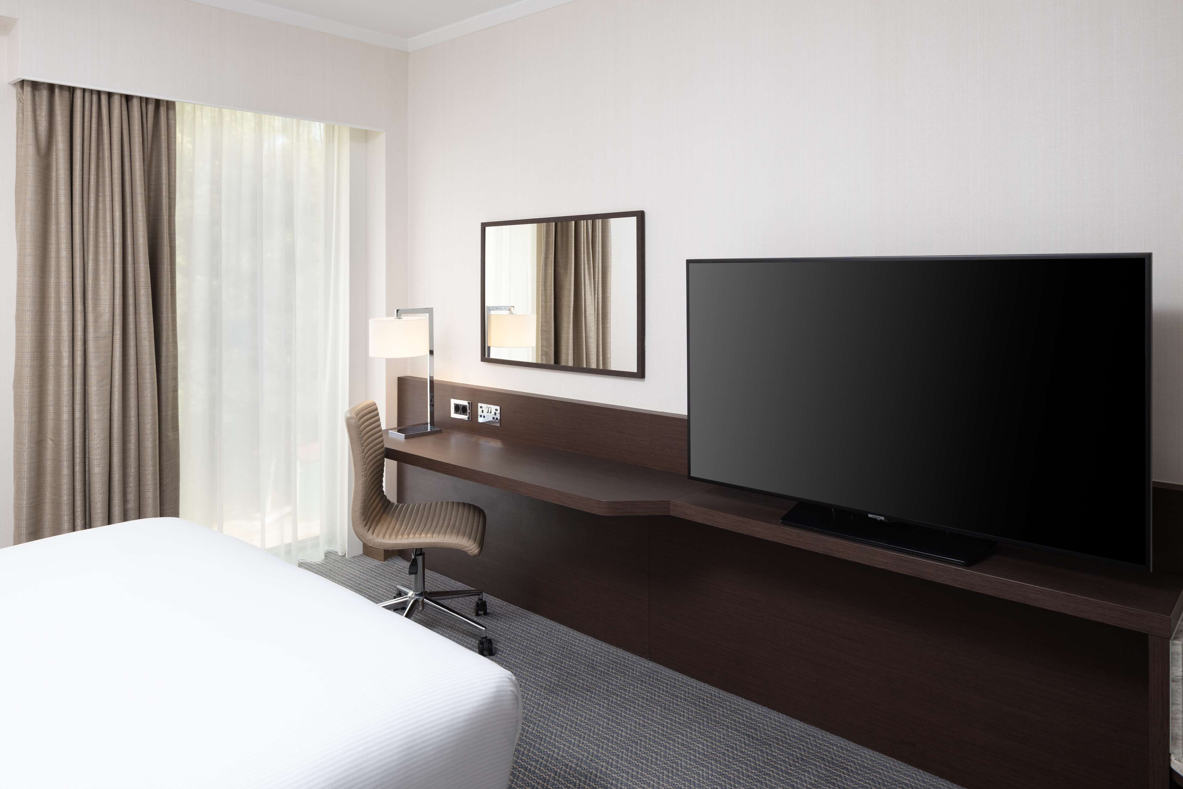 A hotel room with a large bed, a desk with a flat-screen TV, a chair, and a mirror.