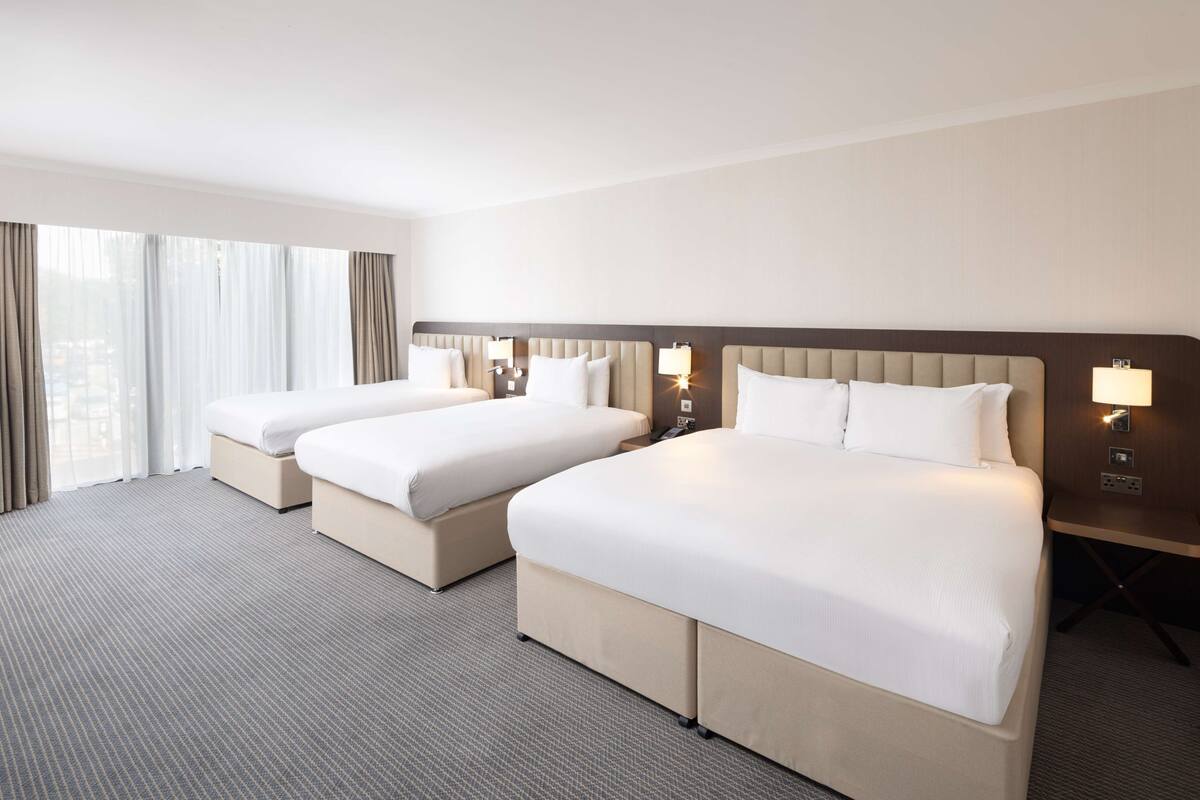 Hotellihuone, jossa on kaksi sänkyä, suuri ikkuna, jossa on verhot, ja yöpöytävalaisimet.