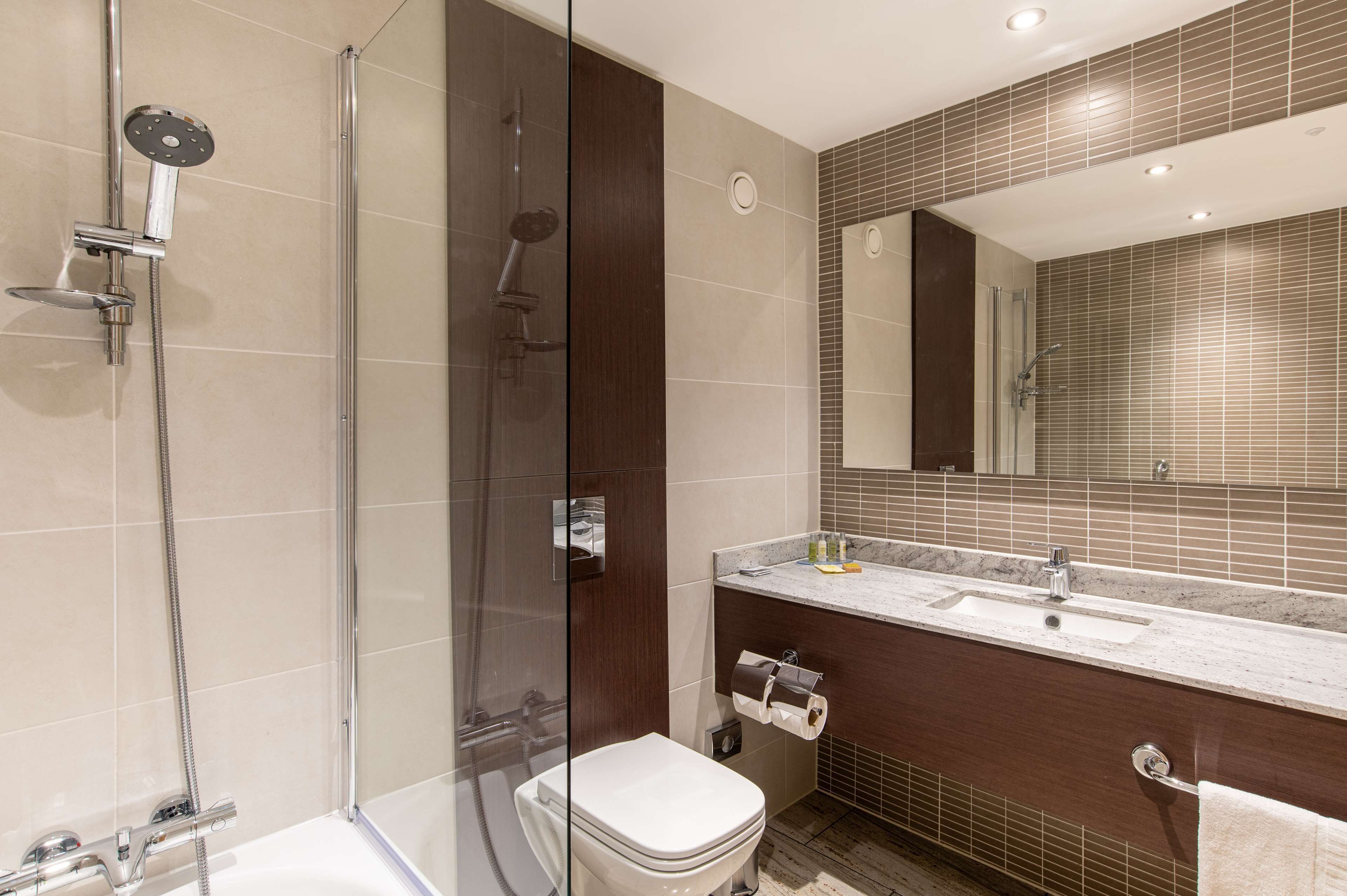 A modern bathroom with a glass-enclosed shower, a separate toilet, and a vanity with a sink and mirror.