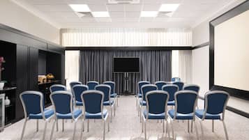 A conference room with rows of blue chairs, a large screen, and a projector.