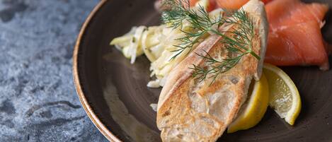 A plate with smoked salmon, a slice of bread, a lemon wedge, and a sprig of dill.