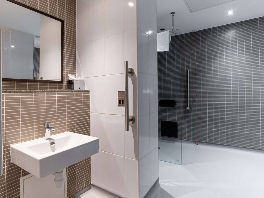 Un baño moderno con lavamanos blanco, un espejo grande y cabina de ducha con paredes de vidrio.