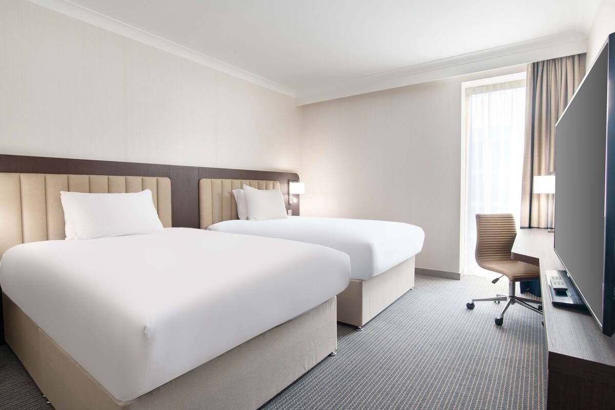Hotellihuone, jossa on kaksi sänkyä, työpöytä, tuoli ja televisio.