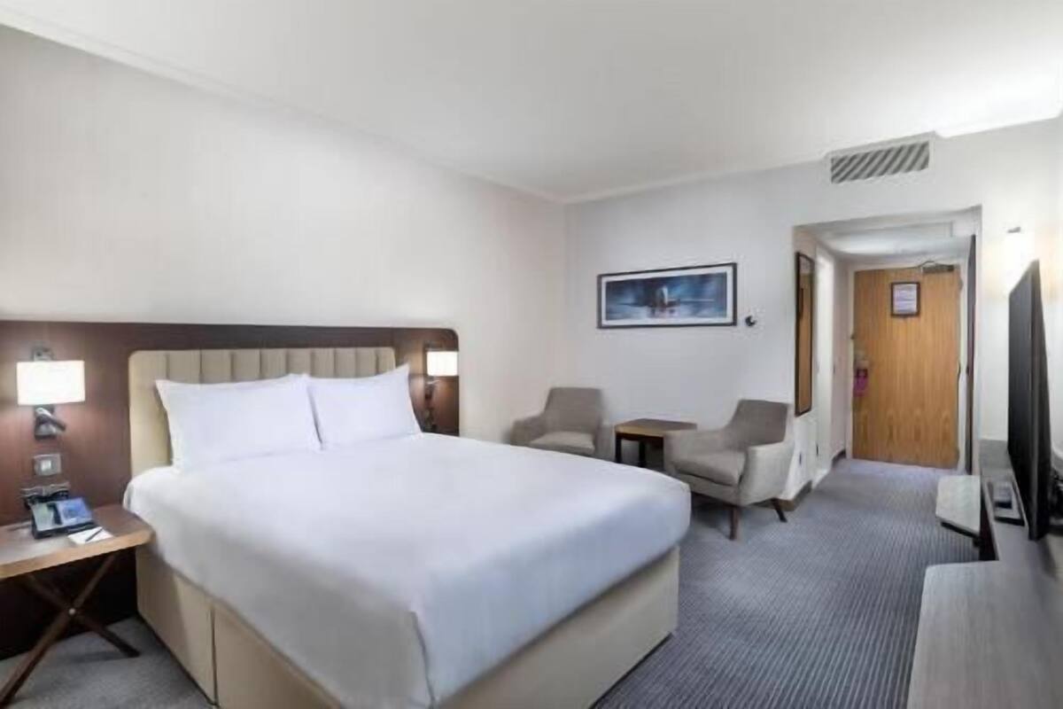 Hotellihuone, jossa on suuri sänky, työpöytä lampun kanssa, kaksi nojatuolia, pieni pöytä ja televisio.