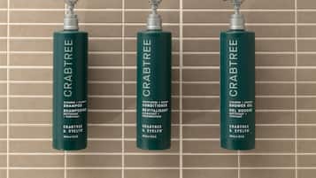 Three bottles of Crabtree & Evelyn shampoo, conditioner, and shower gel against a tiled wall.