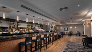 A bar area with a long counter, multiple bar stools, and a variety of bottles and glasses on shelves.