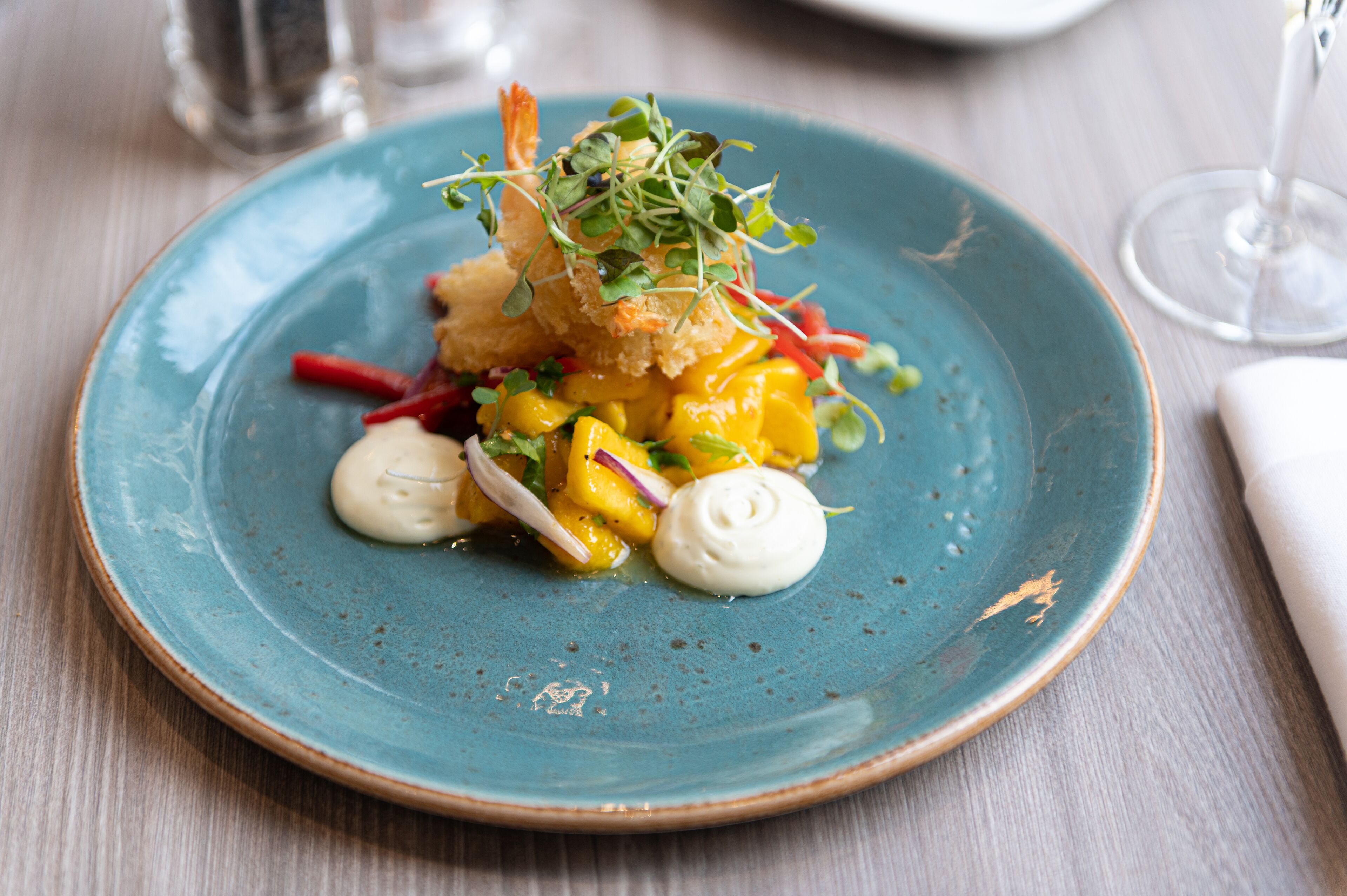 A blue plate with a dish of food, including mango and possibly shrimp, on a wooden table.