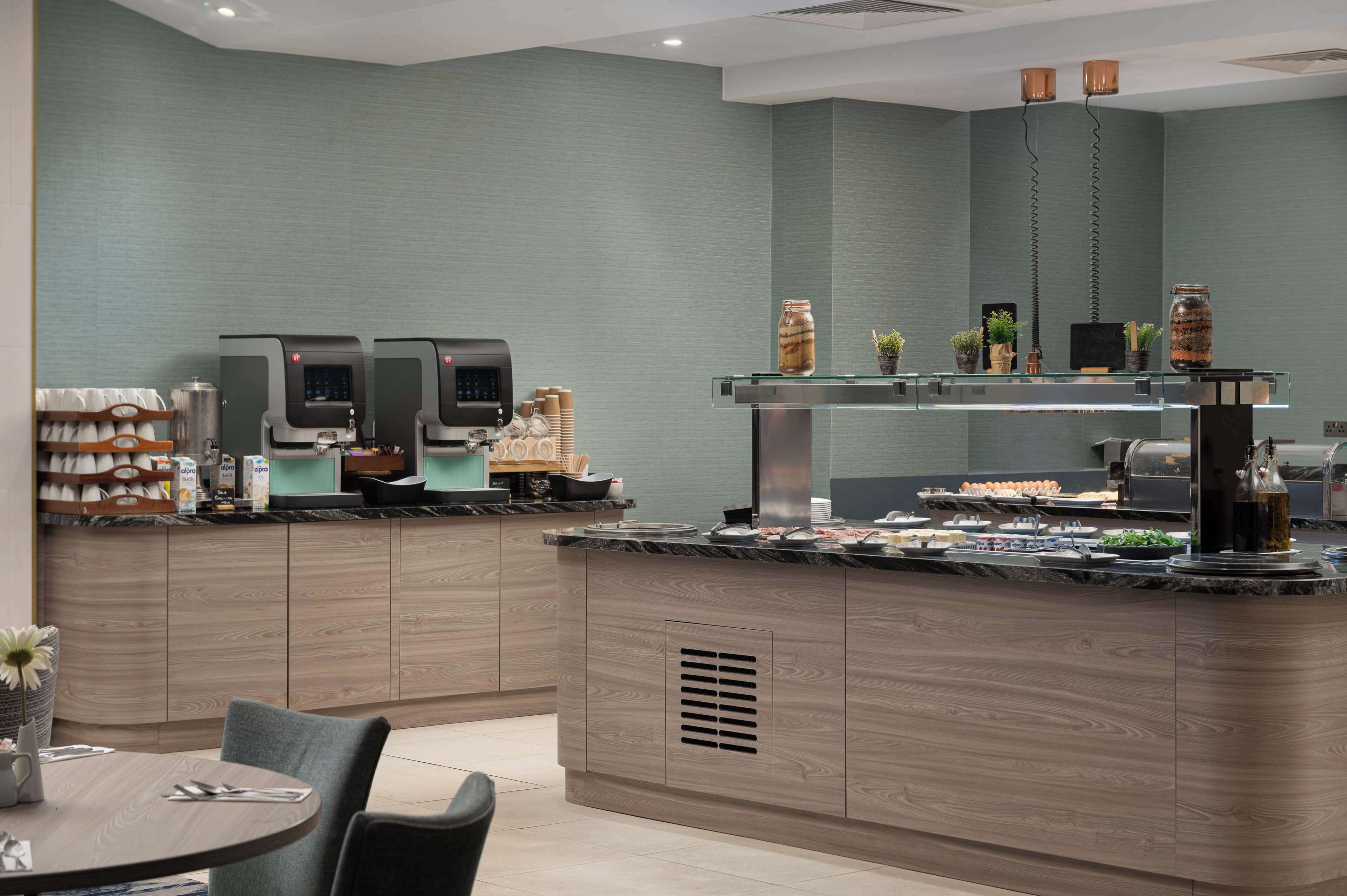 A modern cafe with a wooden counter, coffee machines, and a variety of food items displayed.