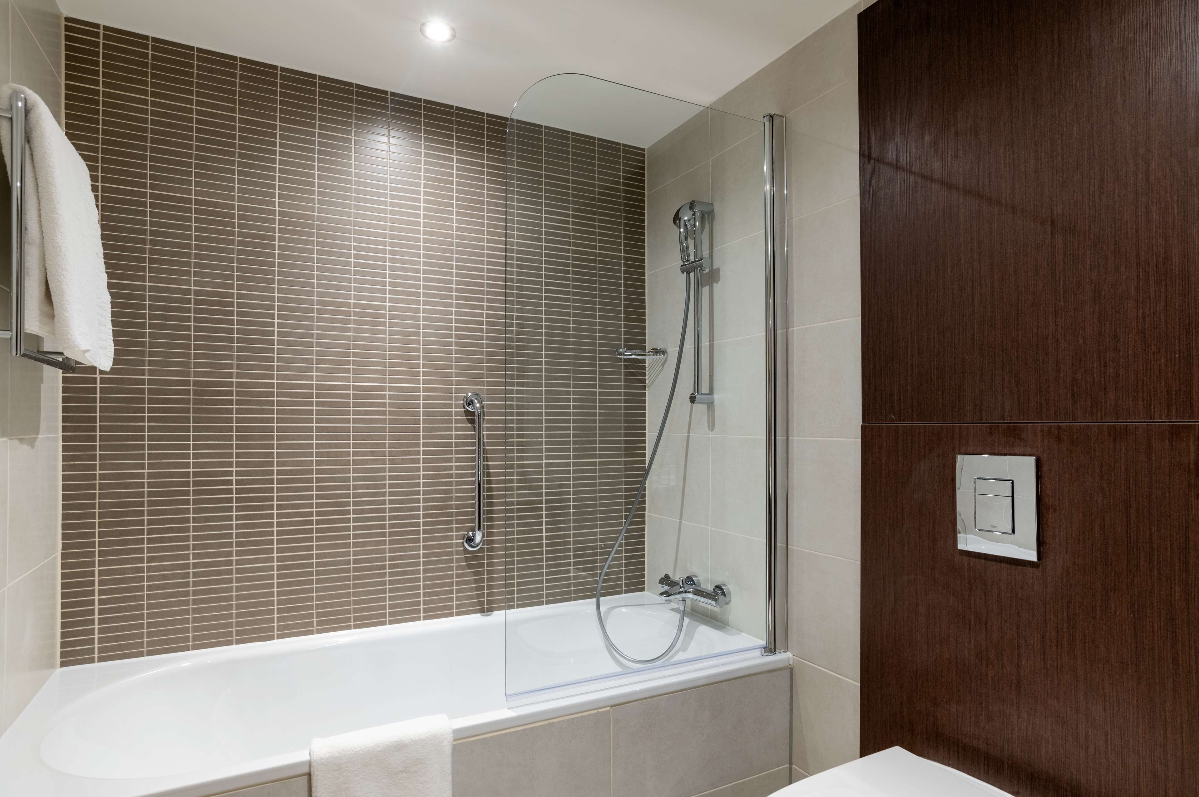 A modern bathroom with a glass-enclosed shower, a white bathtub, and a towel rack.