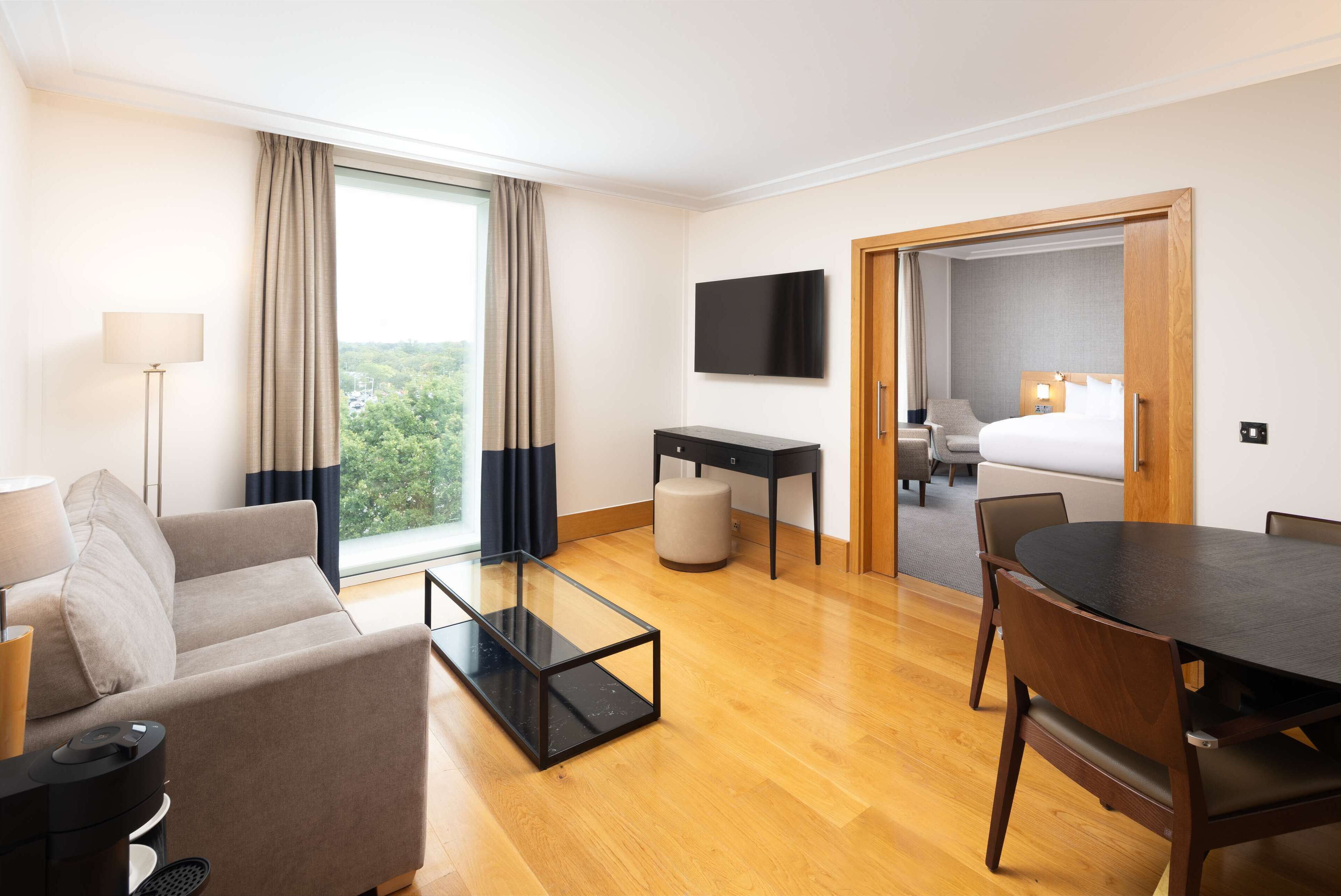 A hotel room with a sofa, a coffee table, a TV, a desk, a bed, and a dining table with chairs.