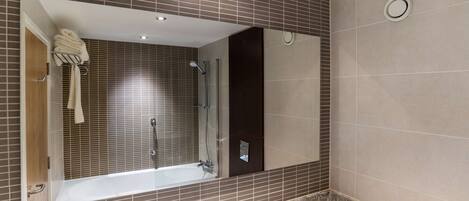 A modern bathroom with a large mirror, a bathtub, a shower, and a marble countertop with toiletries.