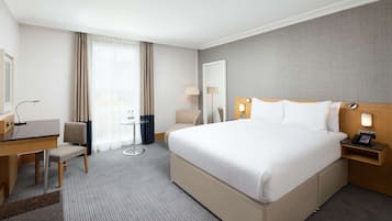 Una habitación de hotel con una cama grande, un escritorio con silla, una mesita pequeña y una lámpara.