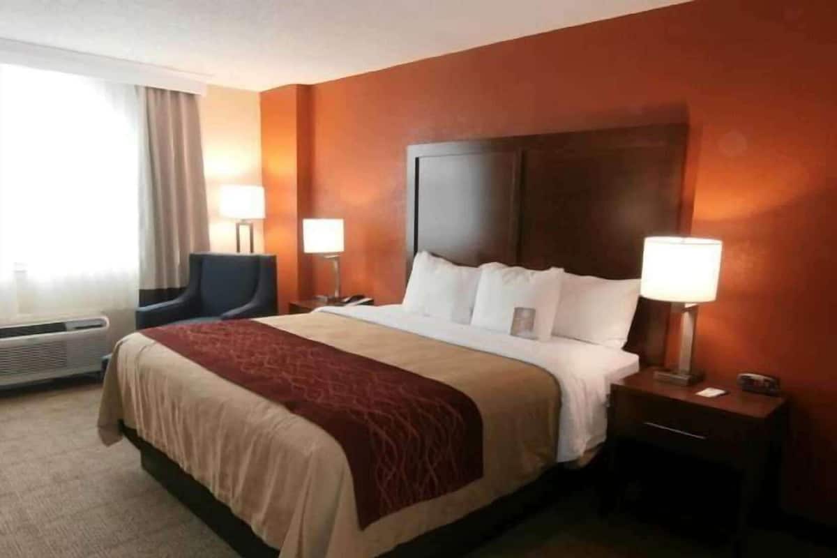 Een hotelkamer met een groot bed, twee nachtkastjes met lampen, een stoel en een raam met gordijnen.