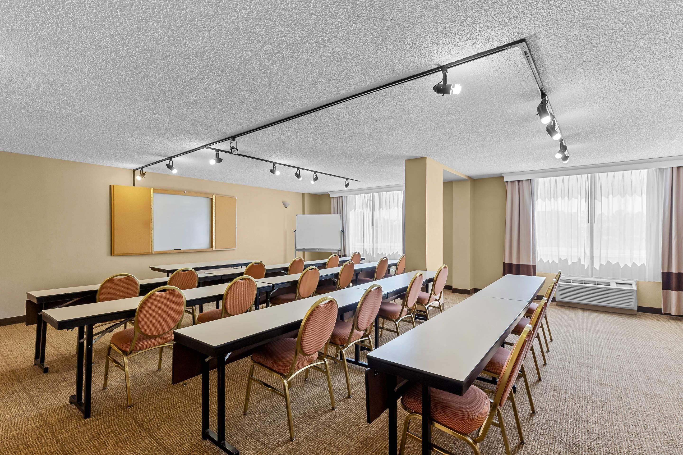 Un salón de conferencias con mesas largas, sillas, una pizarra y una pantalla de proyector.