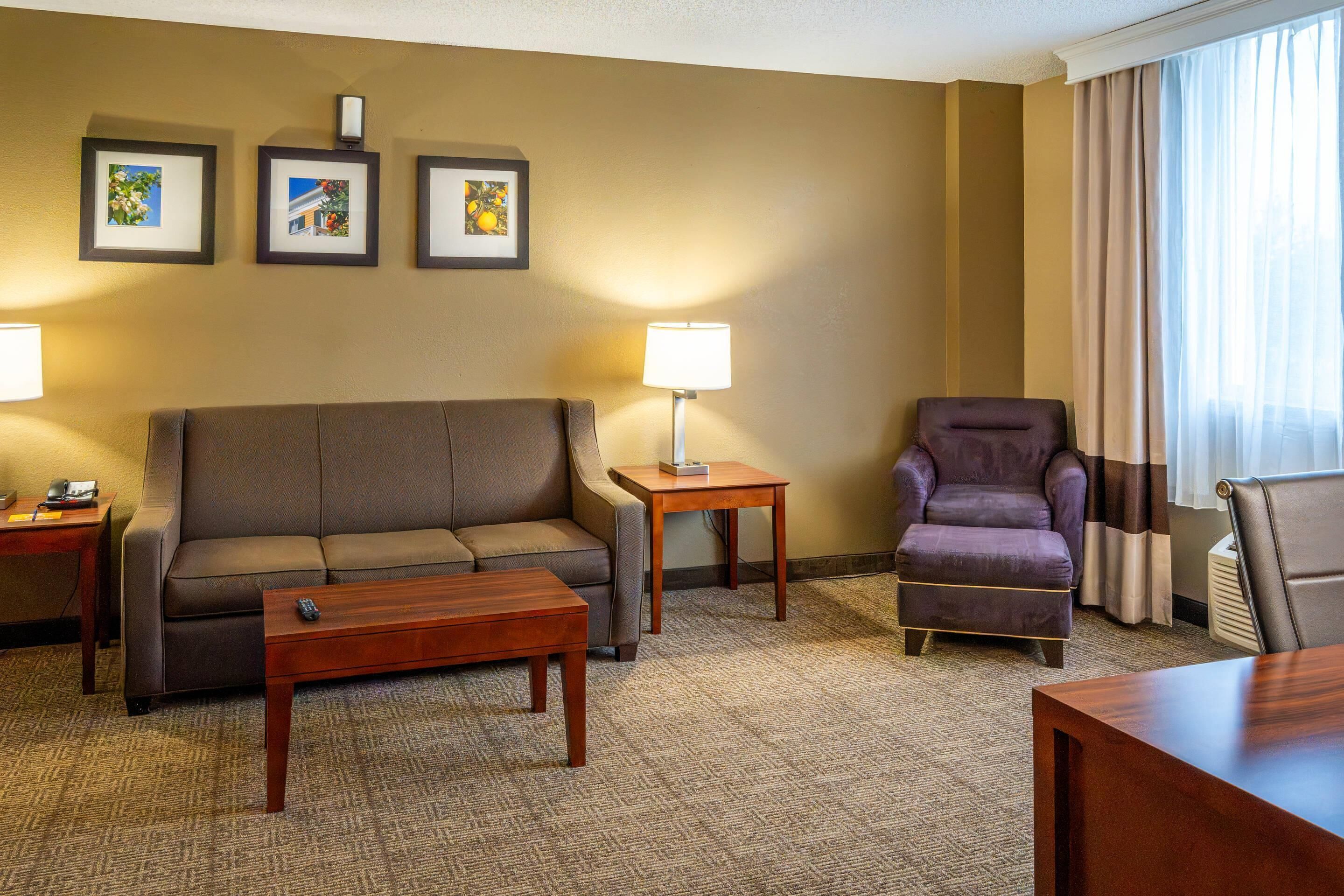A hotel room with a sofa, armchair, coffee table, lamp, and framed pictures on the wall.