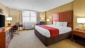 A hotel room with a large bed, a desk with a chair, a TV, and two lamps.
