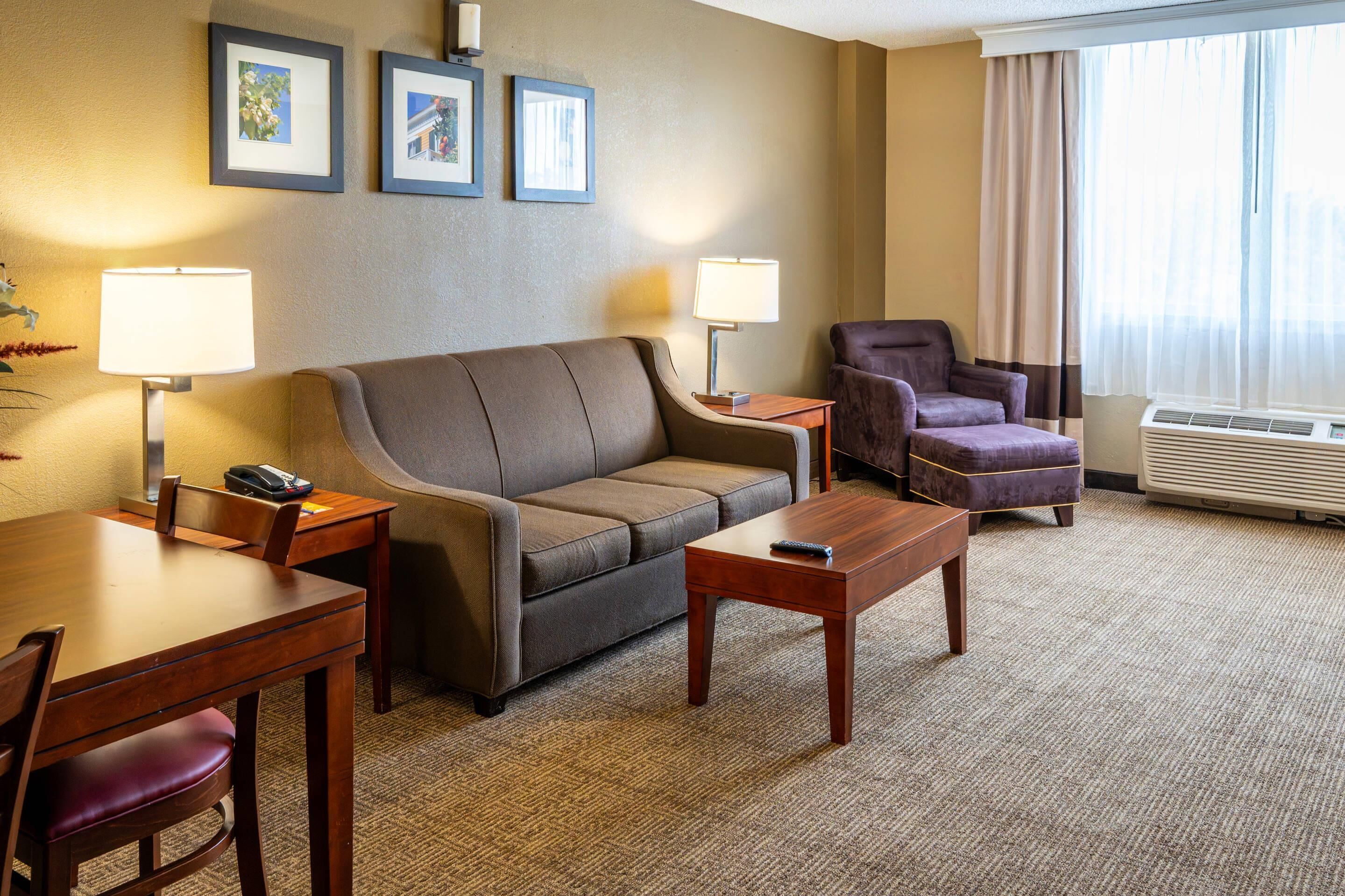 Una habitación de hotel con sofá, sillón, mesa de comedor, lámparas y cuadros en la pared.