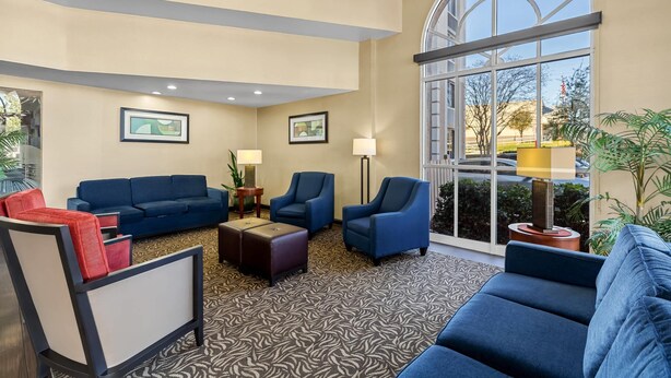 A hotel lobby with a blue sofa set, a red chair, a patterned carpet, and large windows offering a view of the outdoors.